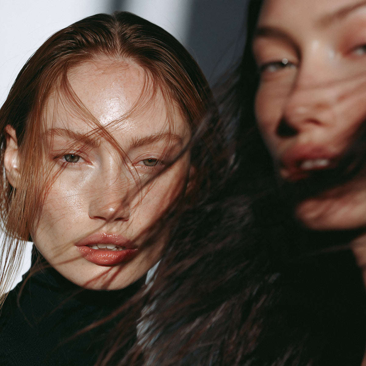 Two models with hair blowing across their faces